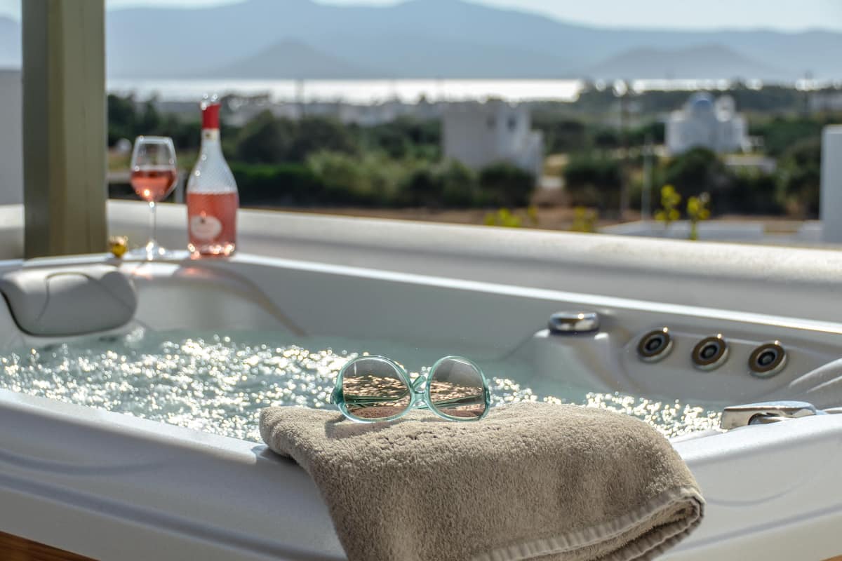 Ein Whirlpool mit Gläsern und einer Flasche, ein Handtuch und die Aussicht auf Grünflächen und Gebäude.