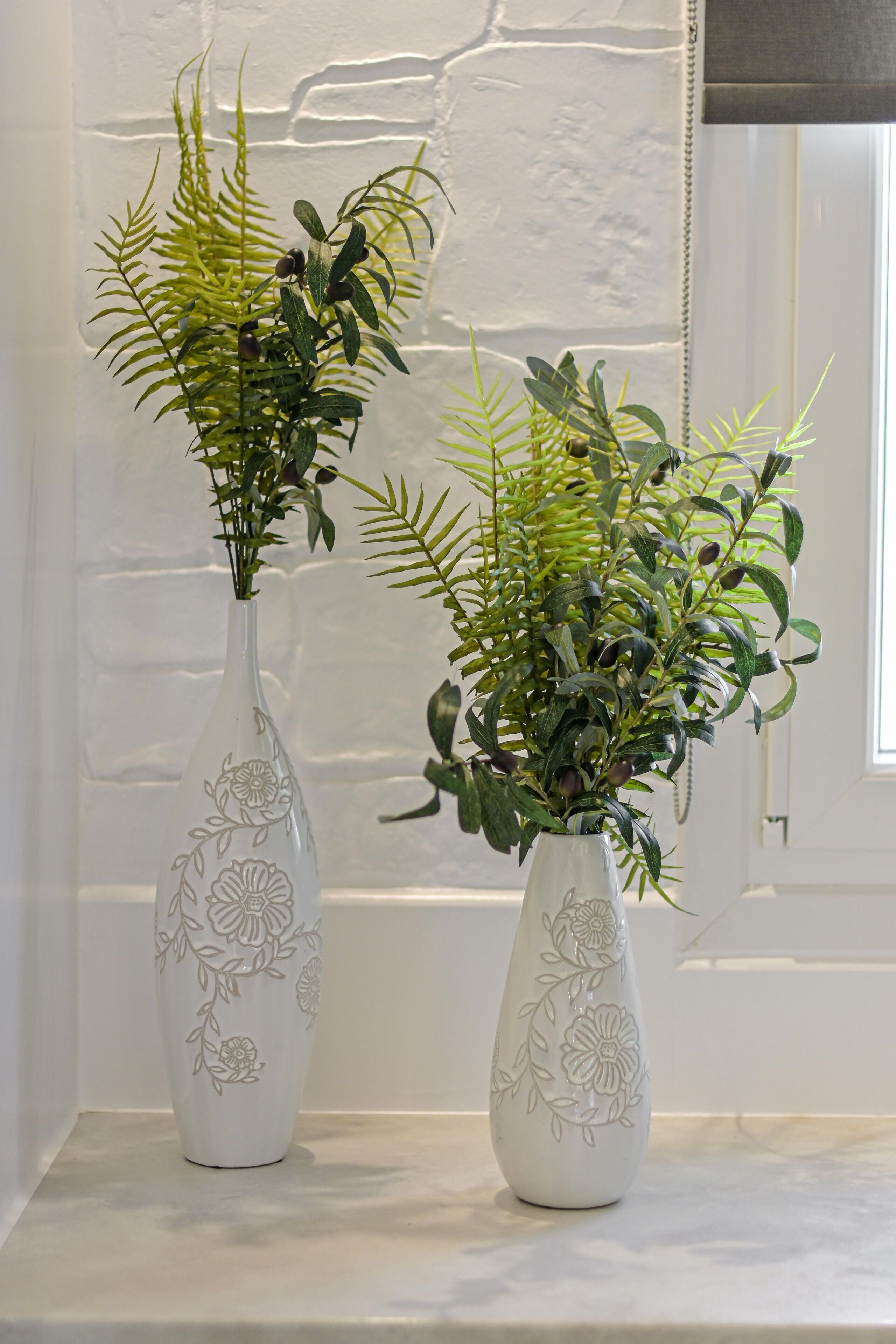 Two white vases with floral designs on a white shelf against a white wall.