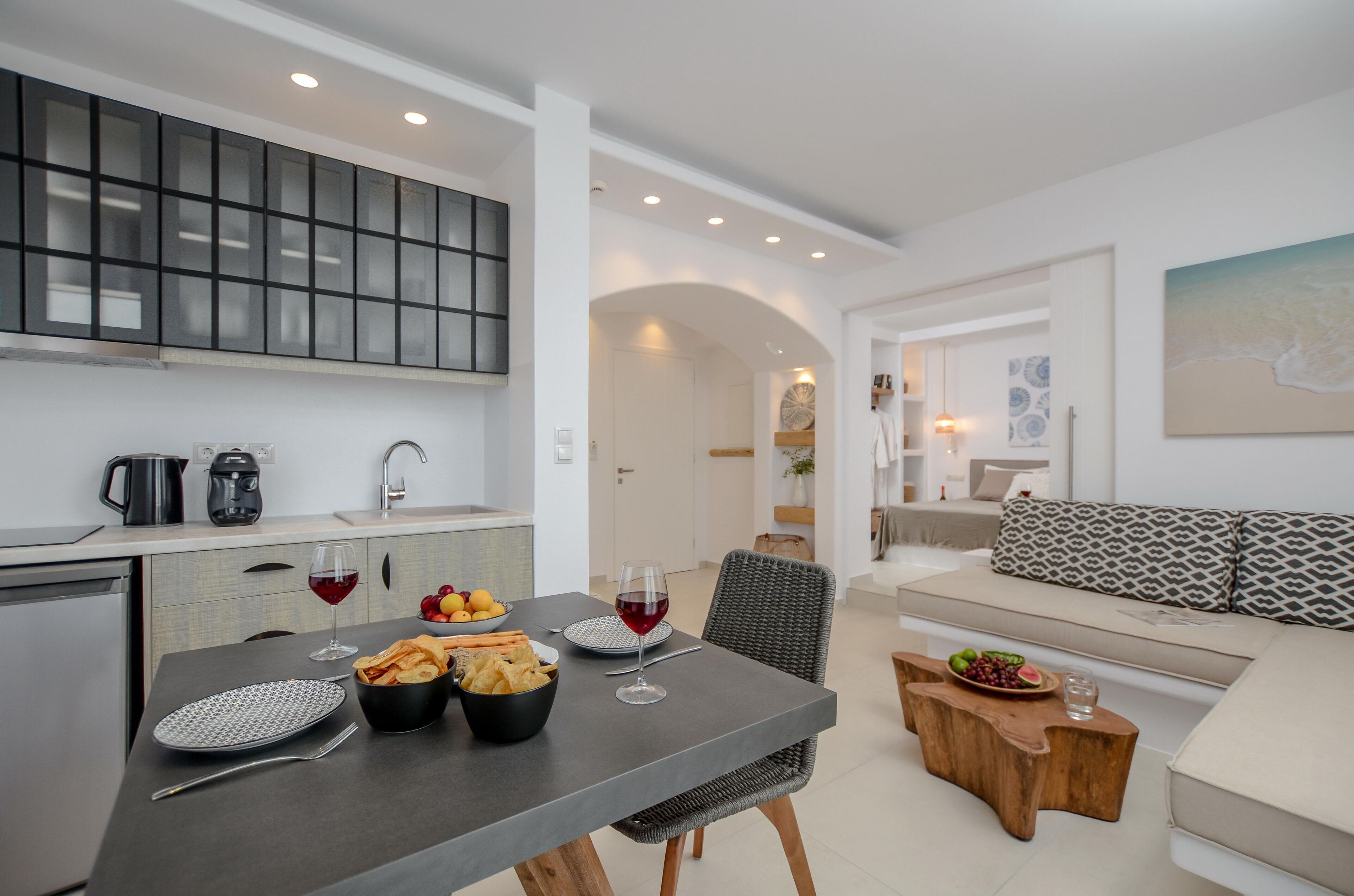 A modern kitchen with a dining area, featuring a grey table, black bowl, and wine glasses.
