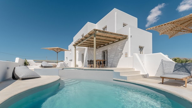 Un área moderna junto a la piscina con una piscina azul cristalina, arquitectura blanca y mobiliario exterior.