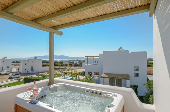 A hot tub with a bottle of wine and a glass, overlooking a pool and white buildings with a clear sky. - Sea & Olives Holiday Villas and Suites (Naxos)