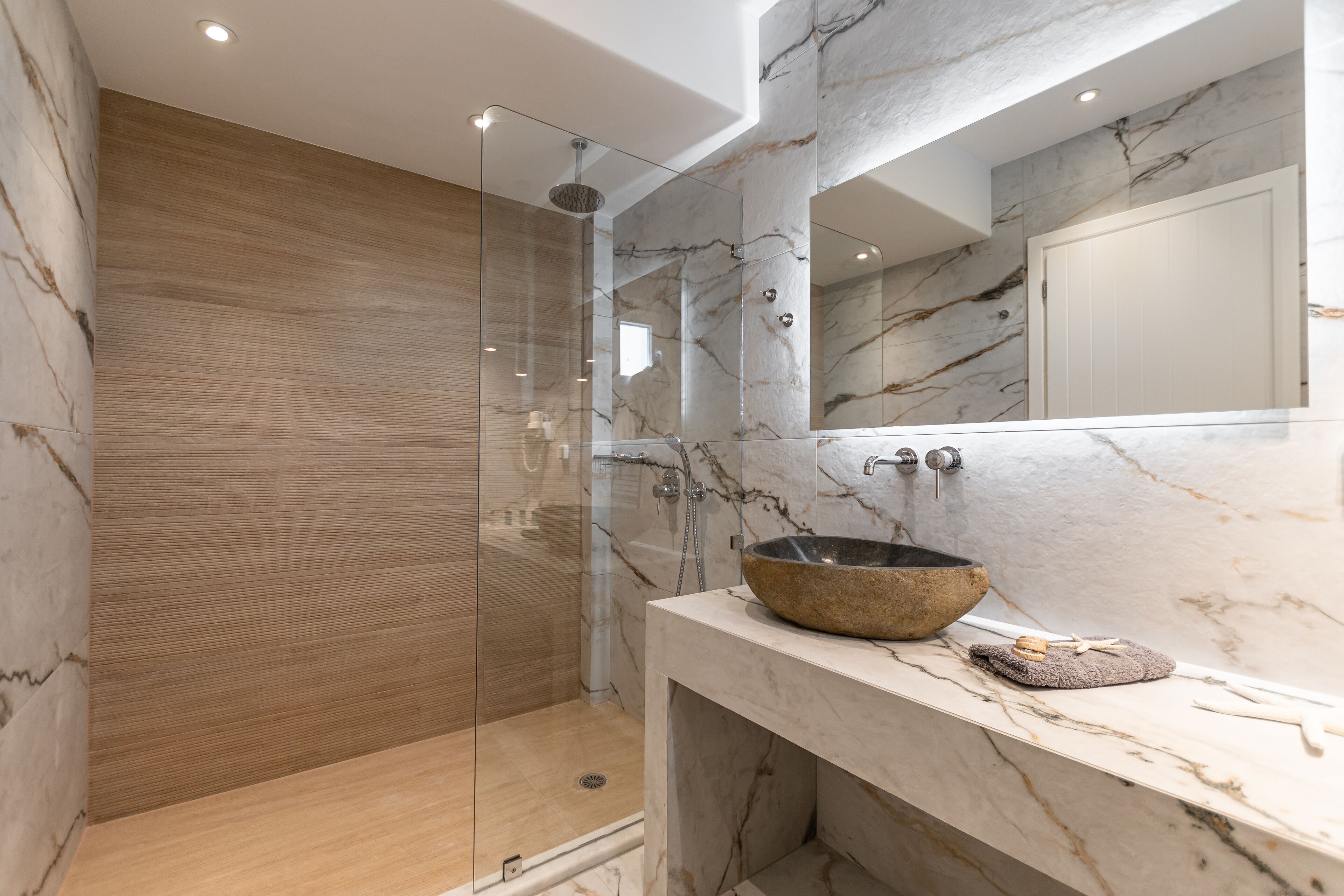 A modern bathroom with a glass-enclosed shower, a marble sink, and a wooden vanity.