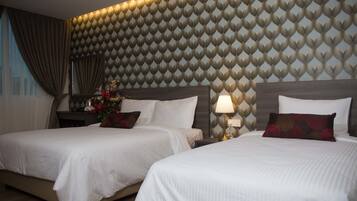 A hotel room with two beds, a decorative wall, and a nightstand with a lamp.
