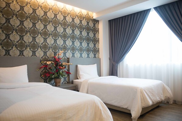 Una habitación de hotel con dos camas, un adorno en la pared, una mesita de noche con un florero y una ventana con cortinas.