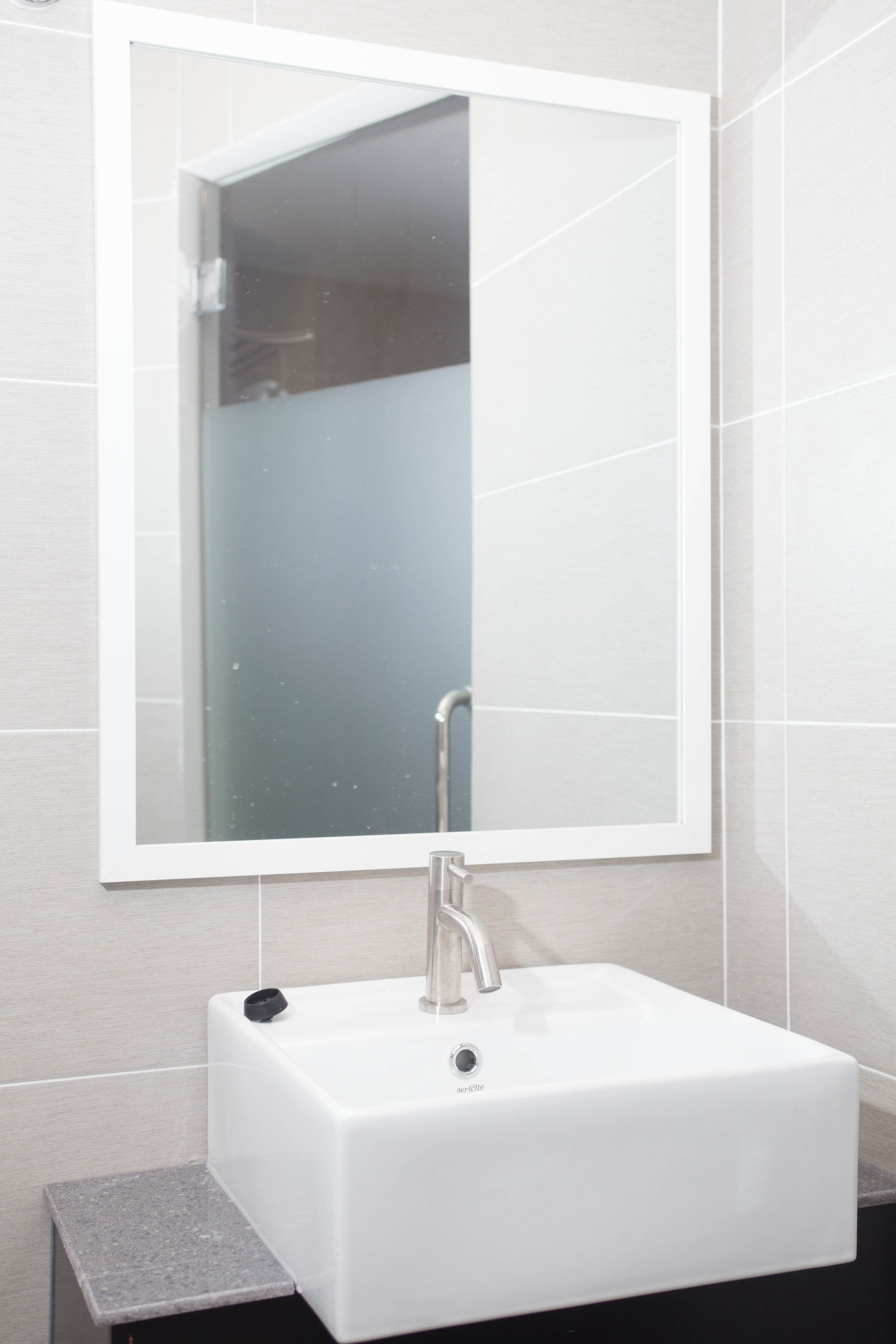 Un bagno con un lavandino bianco, uno specchio e pareti in piastrelle.