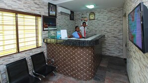 Un área de recepción con una mesa de recepción, dos empleados, un reloj y un televisor en la pared.