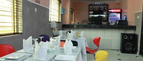 A dining area with tables set for a meal, a bar with various bottles, and a refrigerator.