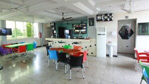 Un comedor amplio con sillas y mesas coloridas, una barra con mostrador, ventiladores de techo y un gran ventanal que proporciona luz natural.