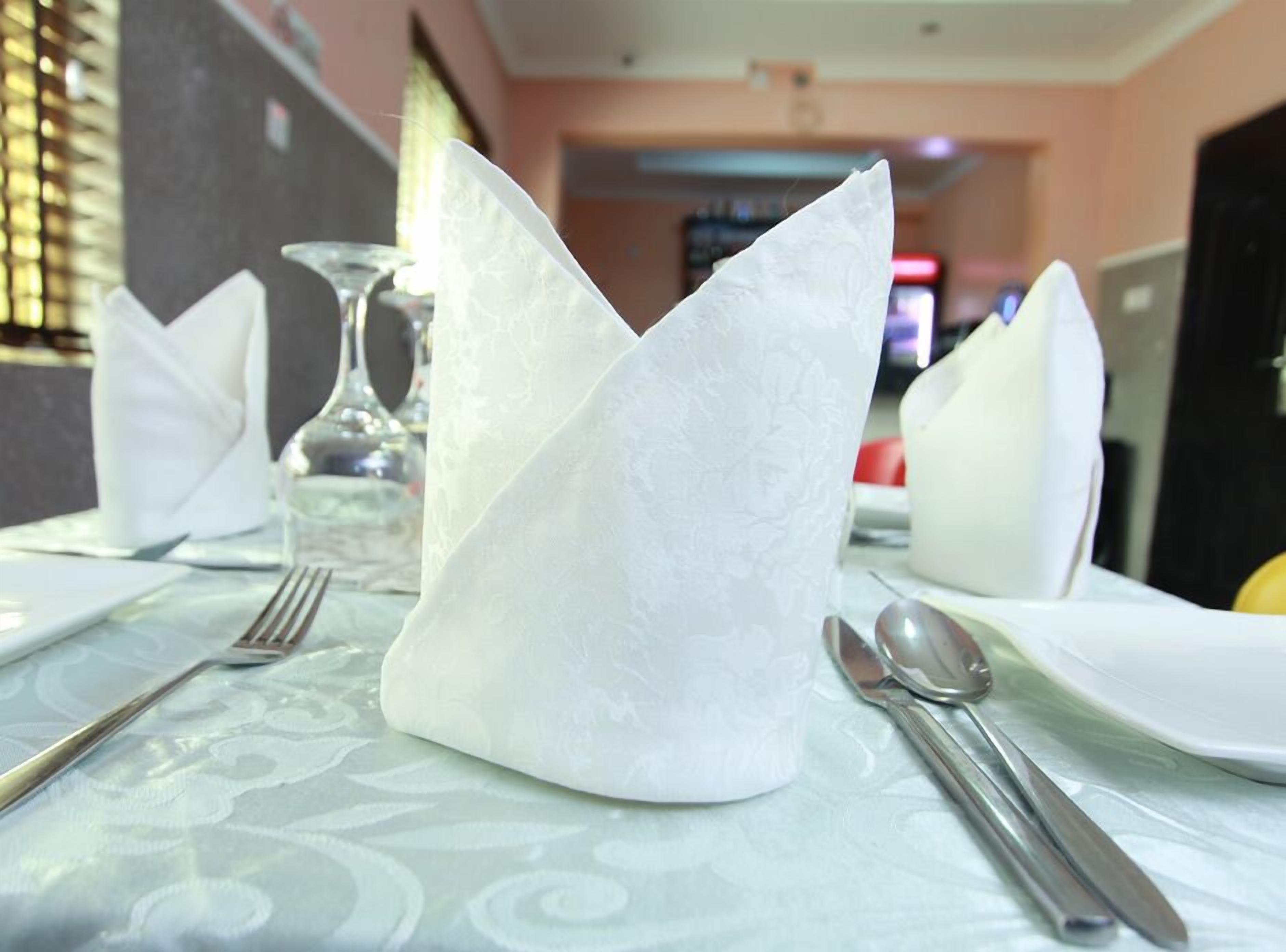 Una mesa dispuesta con servilletas blancas dobladas en forma de barco, cubiertos y una copa.