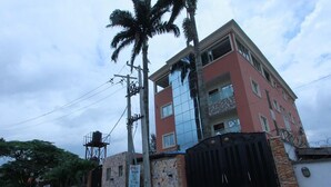 Un edificio de varios pisos con fachada roja, entrada protegida por una reja y una palmera frente a él.