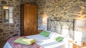 Un dormitorio con pared de piedra, armario de madera y cama con almohadas verdes.
