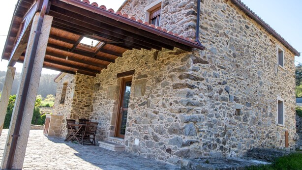 Un edificio de piedra con una pérgola de madera, una puerta y una ventana.
