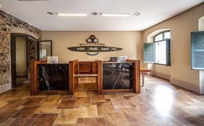 Un mostrador de recepción con fondo de pared de piedra, una mesa de recepción de madera y suelo de baldosas.