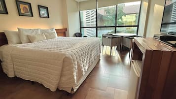 A hotel room with a large bed, a desk with a chair, a television, and a window with blinds.