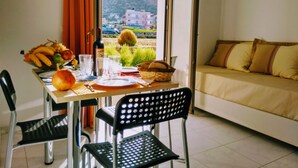 A dining area with a table set for two, a sofa, and a view of a hillside. - Casa Malena (Hersonissos)