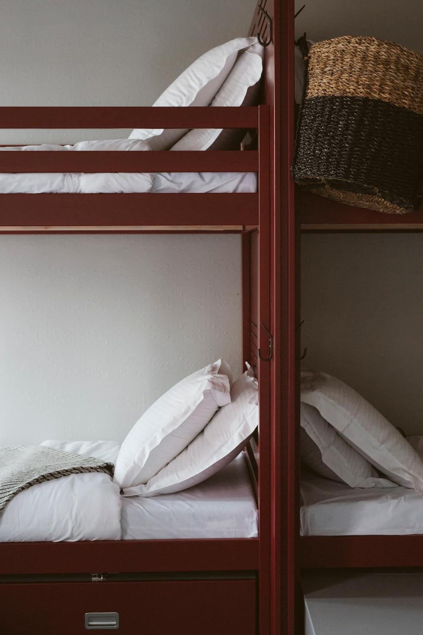 Una cama litera con ropa de cama blanca y una cesta tejida en la parte superior.