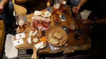 A wooden table with food and drinks, including cheese, meats, and bread, in a casual dining setting.