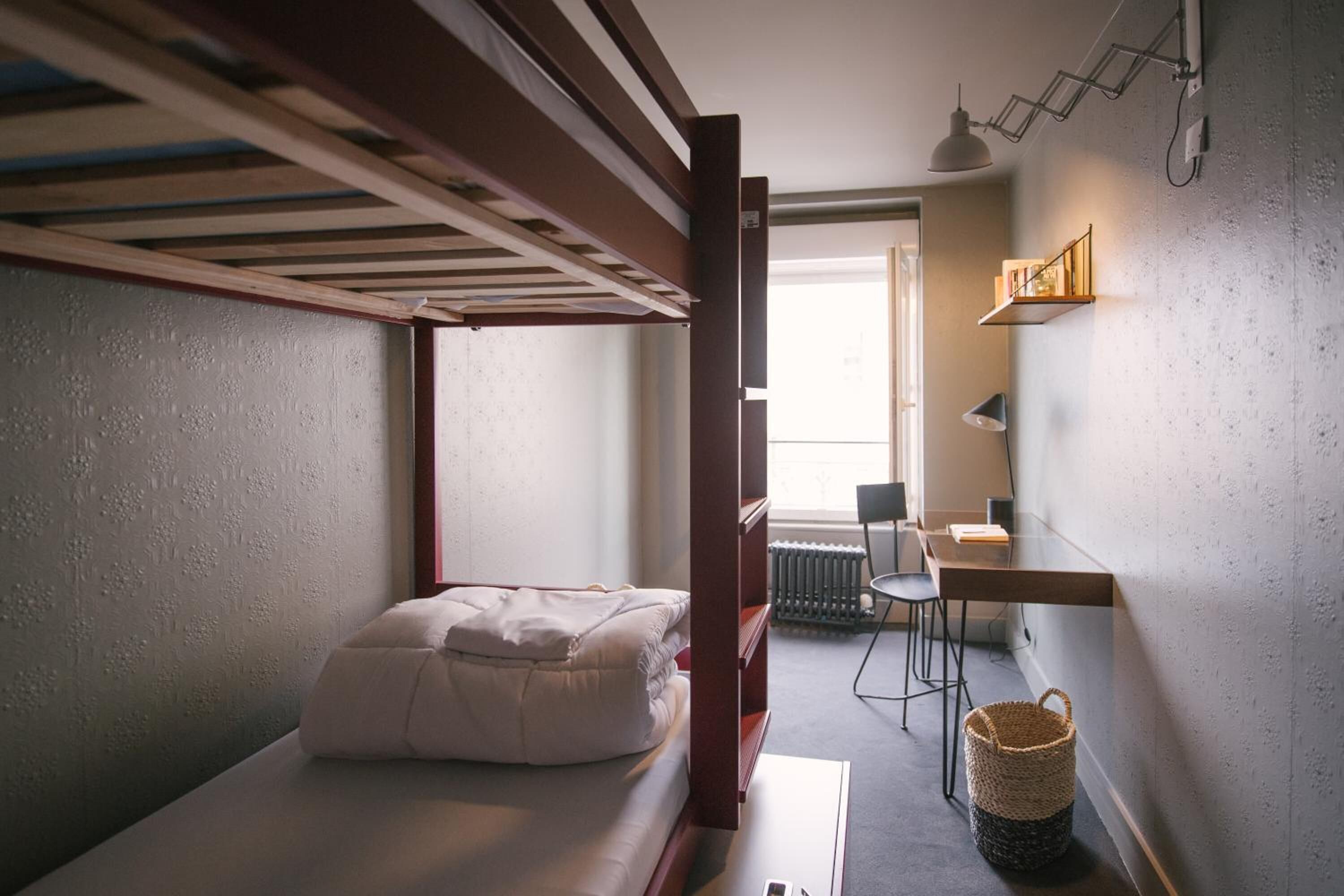 A compact room with a bunk bed, a small desk, a chair, and a window providing natural light.
