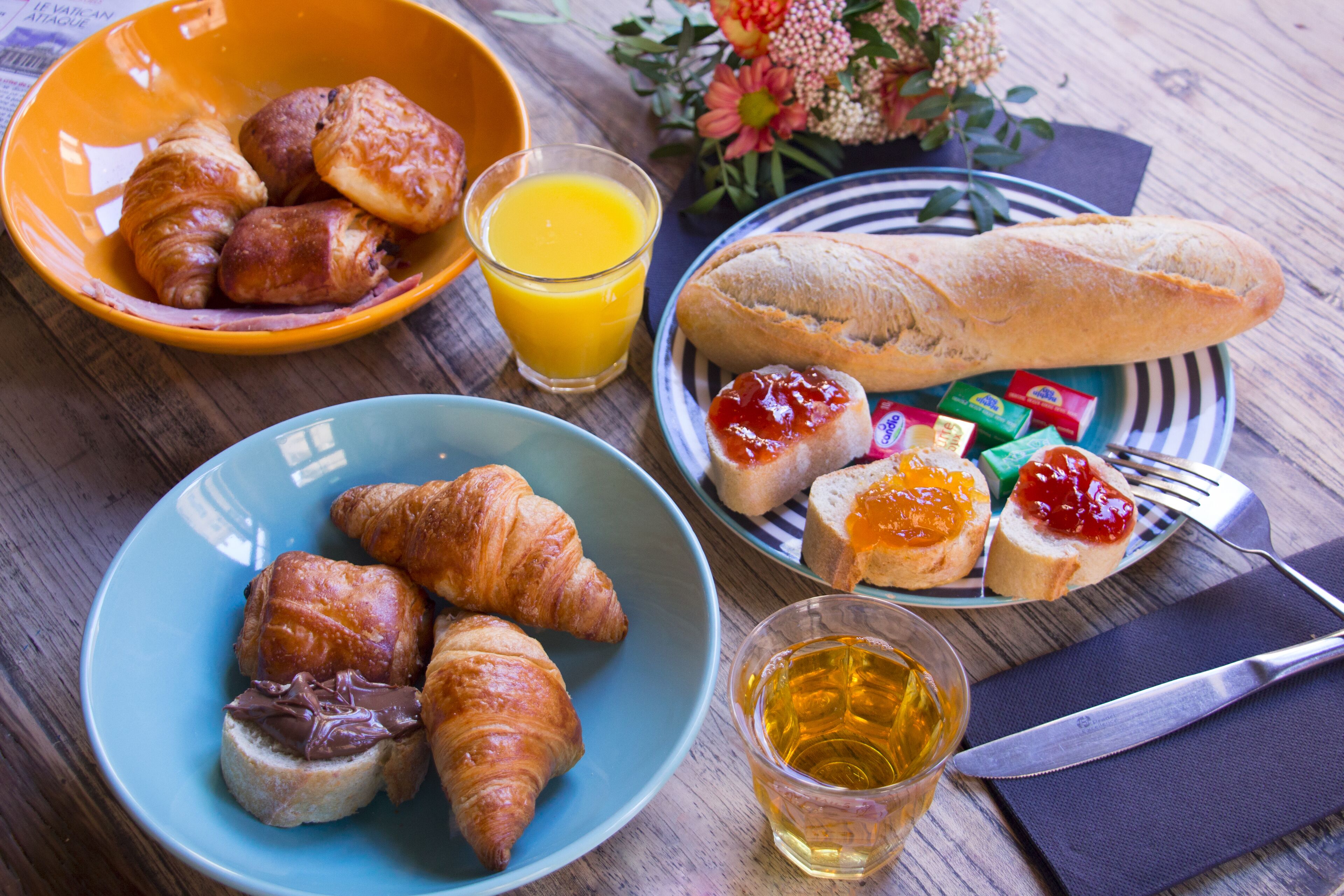 A breakfast setting with croissants, bread, jam, and juice on a wooden table.