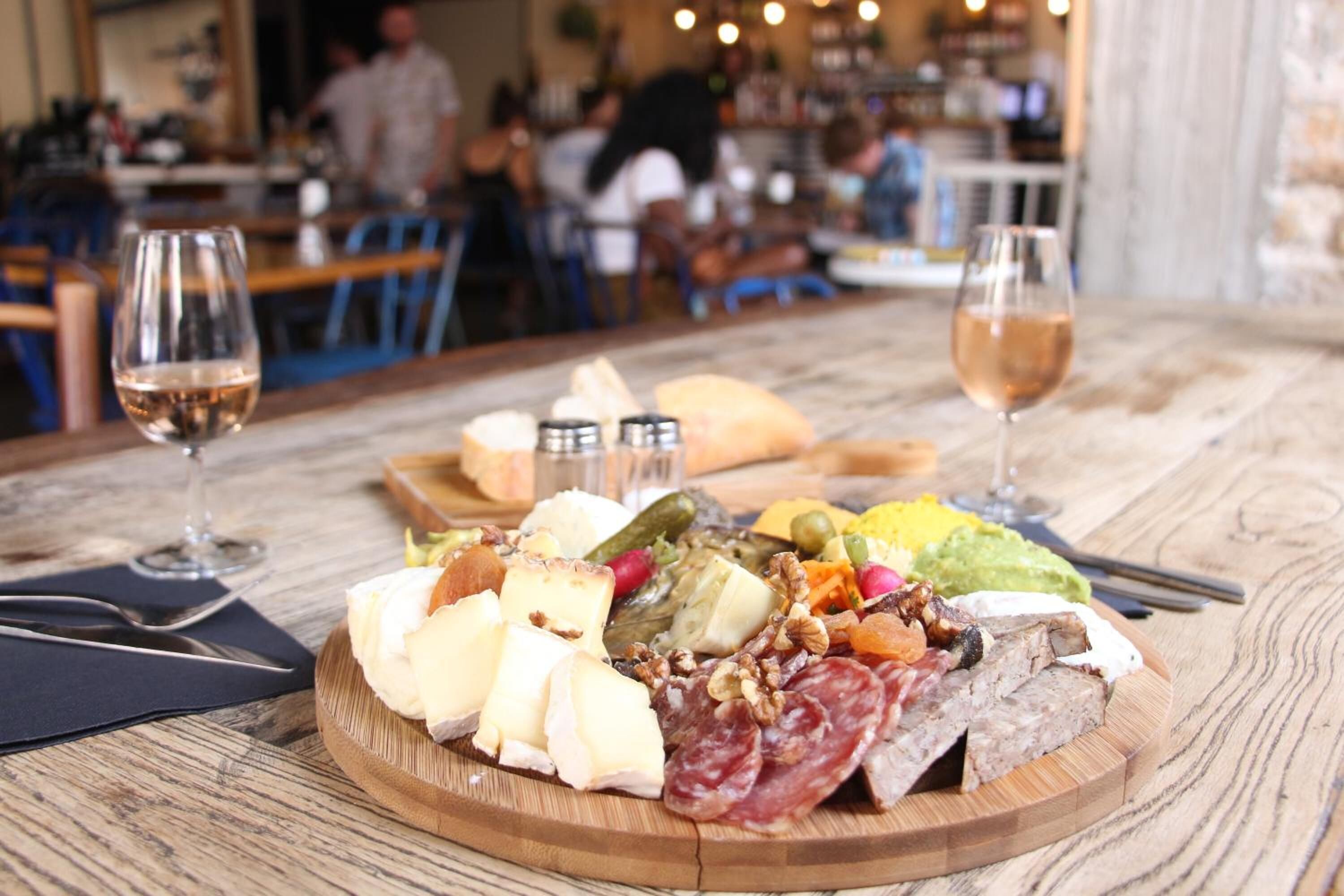 Una tabla de fiambres con diversos quesos, carnes y frutas sobre una mesa de madera en un restaurante.