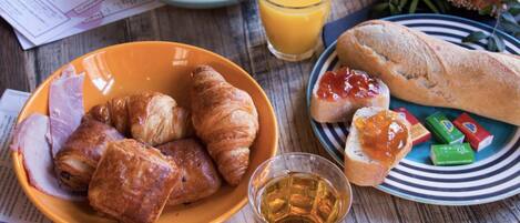 A breakfast setting with croissants, ham, and a glass of juice on a wooden table.