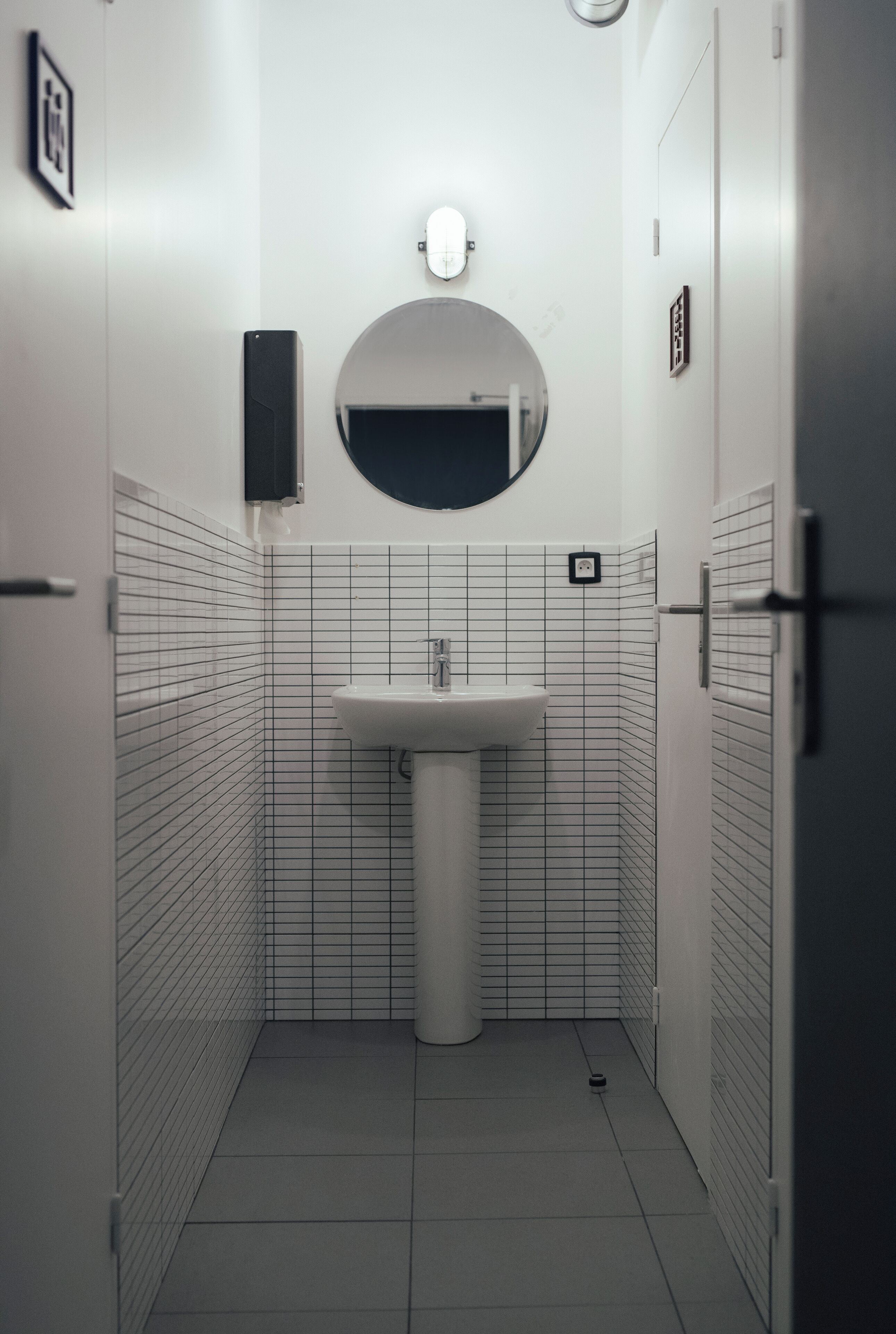 A small, tiled bathroom with a sink, a mirror, and a light fixture.