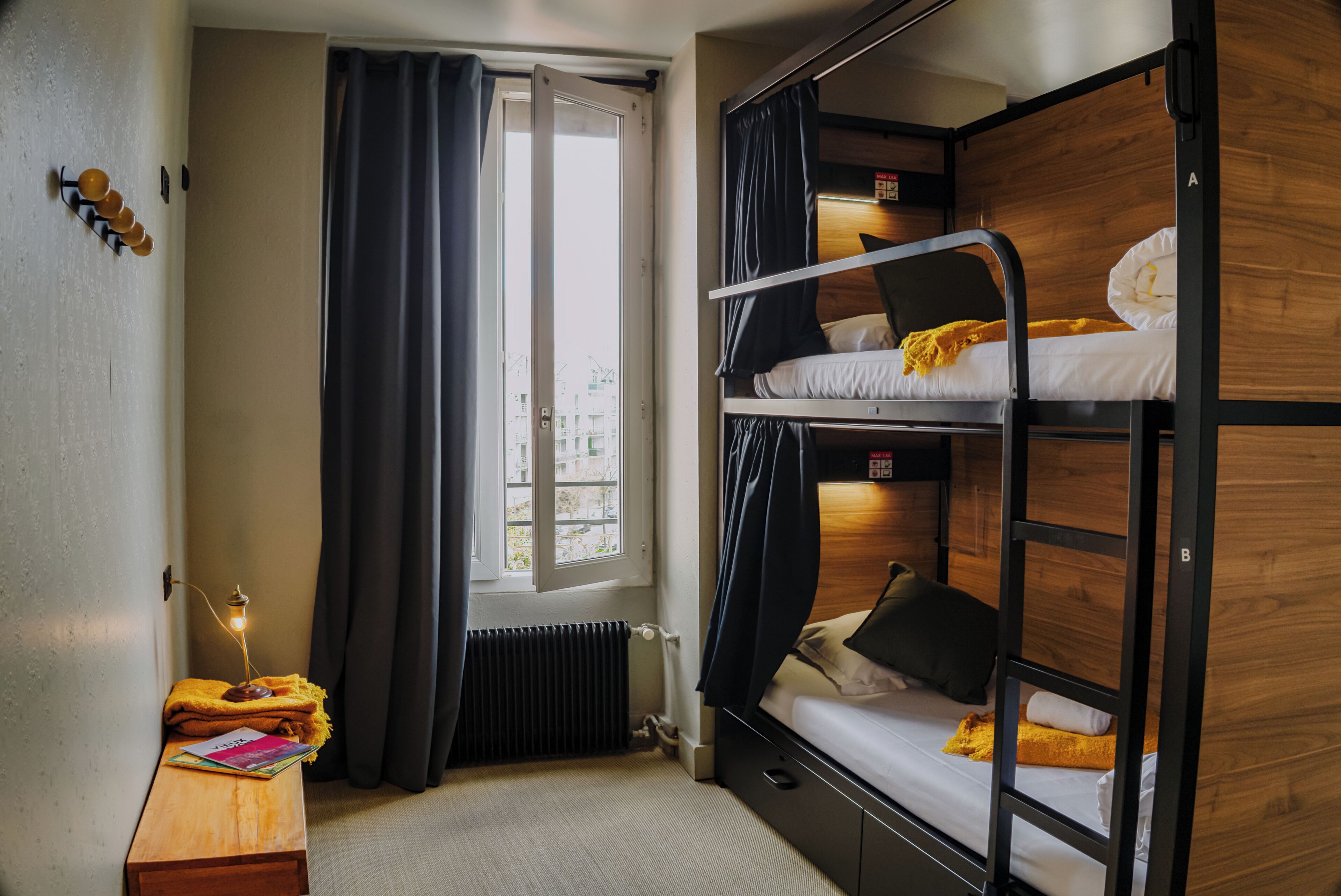 A bunk bed room with a window, a desk with a lamp, and a radiator.