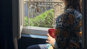 Une personne assise près d’une fenêtre, avec vue sur des immeubles.