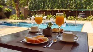 A breakfast setup with orange juice, a plate of fruit, and a small plant on a table by a pool. - Andares Del Agua (Villa Elisa)