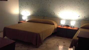 A bedroom with a bed, two bedside tables with lamps, a nightstand, and a wall with a pattern.