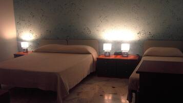 Habitación de hotel con dos camas, cada una con una mesita de noche y una lámpara. Las paredes tienen un diseño con textura salpicada.