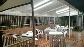 An outdoor patio area with white plastic chairs and tables, a tiled floor, and a metal fence with decorative bars. - Etna Inn (Motta Sant'Anastasia)