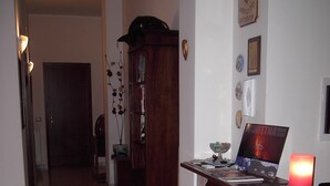 A hallway with a wooden reception desk, a laptop, a pink candle, and a bookshelf. - Etna Inn (Motta Sant'Anastasia)