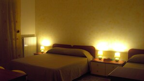 A hotel room with two beds, a nightstand with lamps, a curtain, and a radiator. - Etna Inn (Motta Sant'Anastasia)