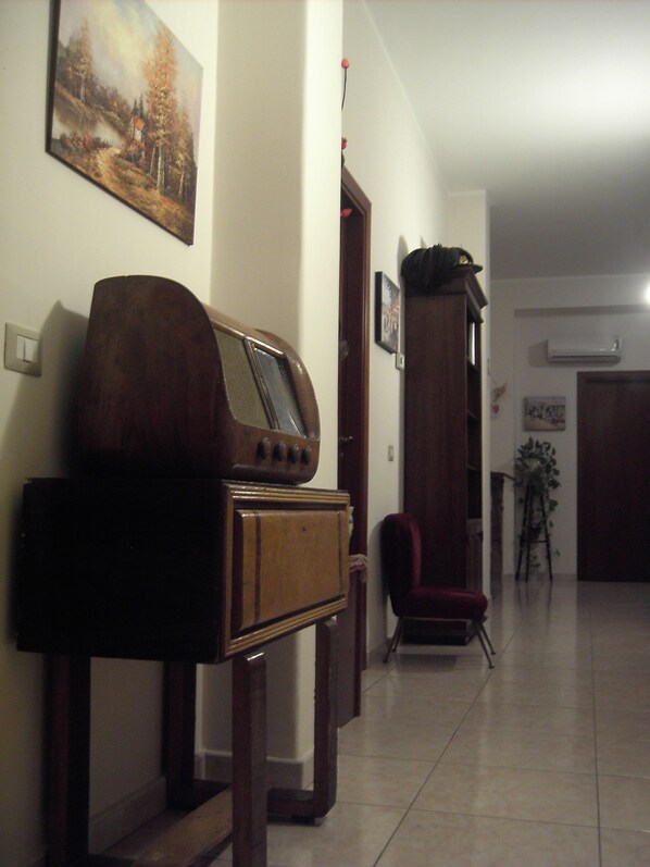 Un salon avec une radio ancienne posée sur un meuble en bois, un fauteuil rouge et un tableau accroché au mur.