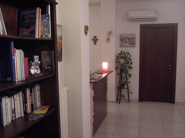 A room with a bookshelf, a desk with a lit candle, a radiator, a wall-mounted air conditioner, and a door.