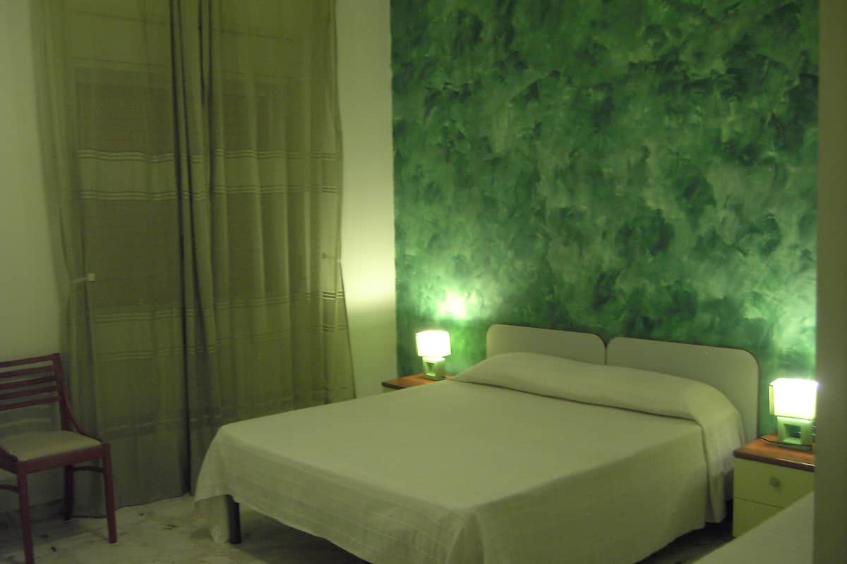 A bedroom with a bed, two bedside tables with lamps, a chair, and a green textured wall.