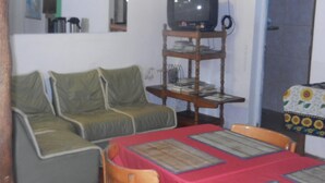 Ein Wohnzimmer mit Fernseher auf einem Holzboden, einer Couch und einem Esstisch mit Unterlaysern.