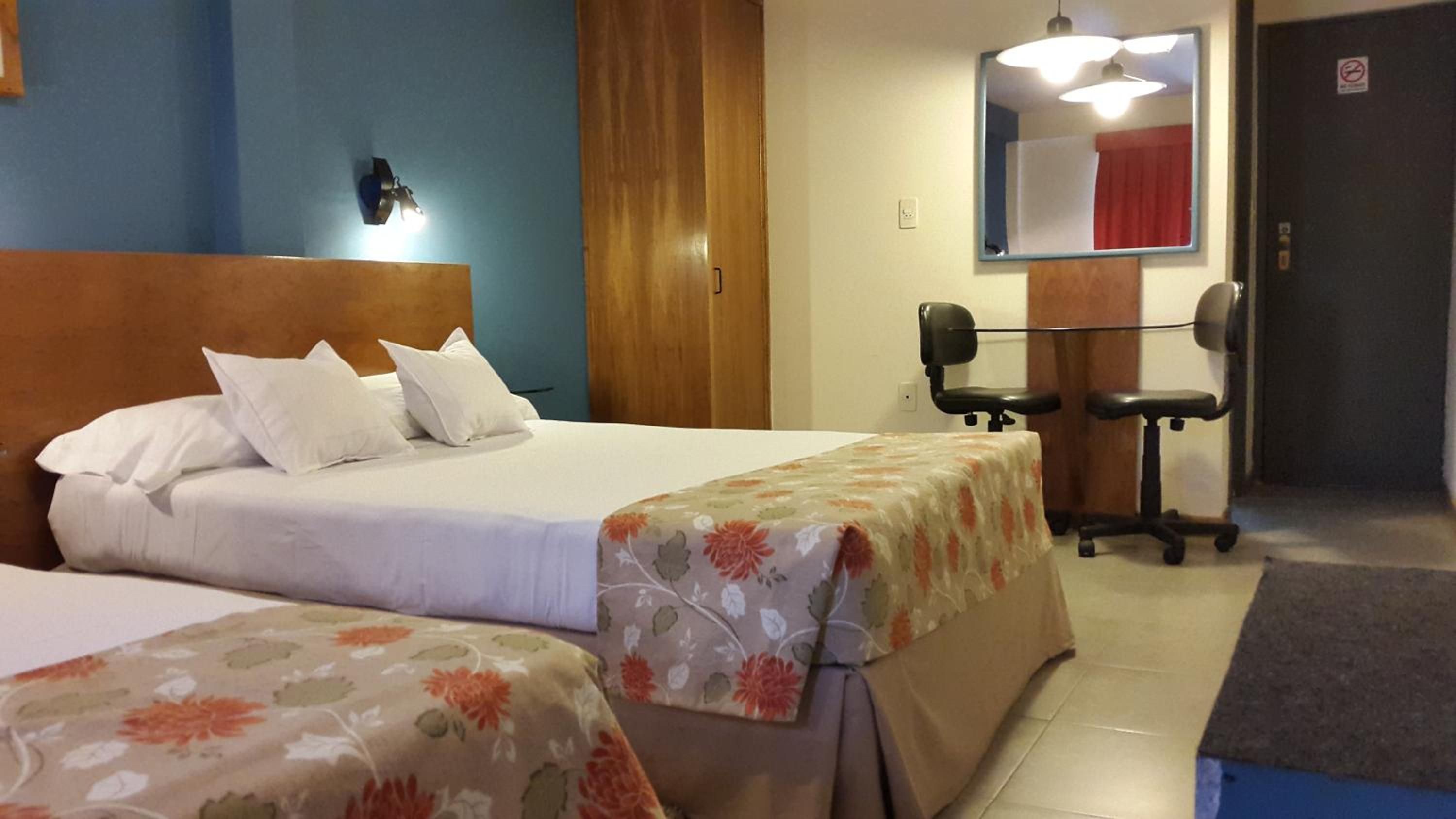 A hotel room with a double bed, a desk with two chairs, a mirror, and a door with a no-smoking sign.