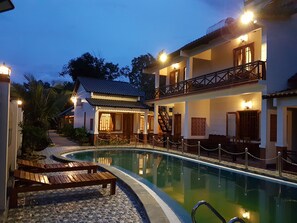 A pool area with wooden loungers and a building with multiple balconies and staircases. - Nhat Huy Bungalow (Phu Quoc)