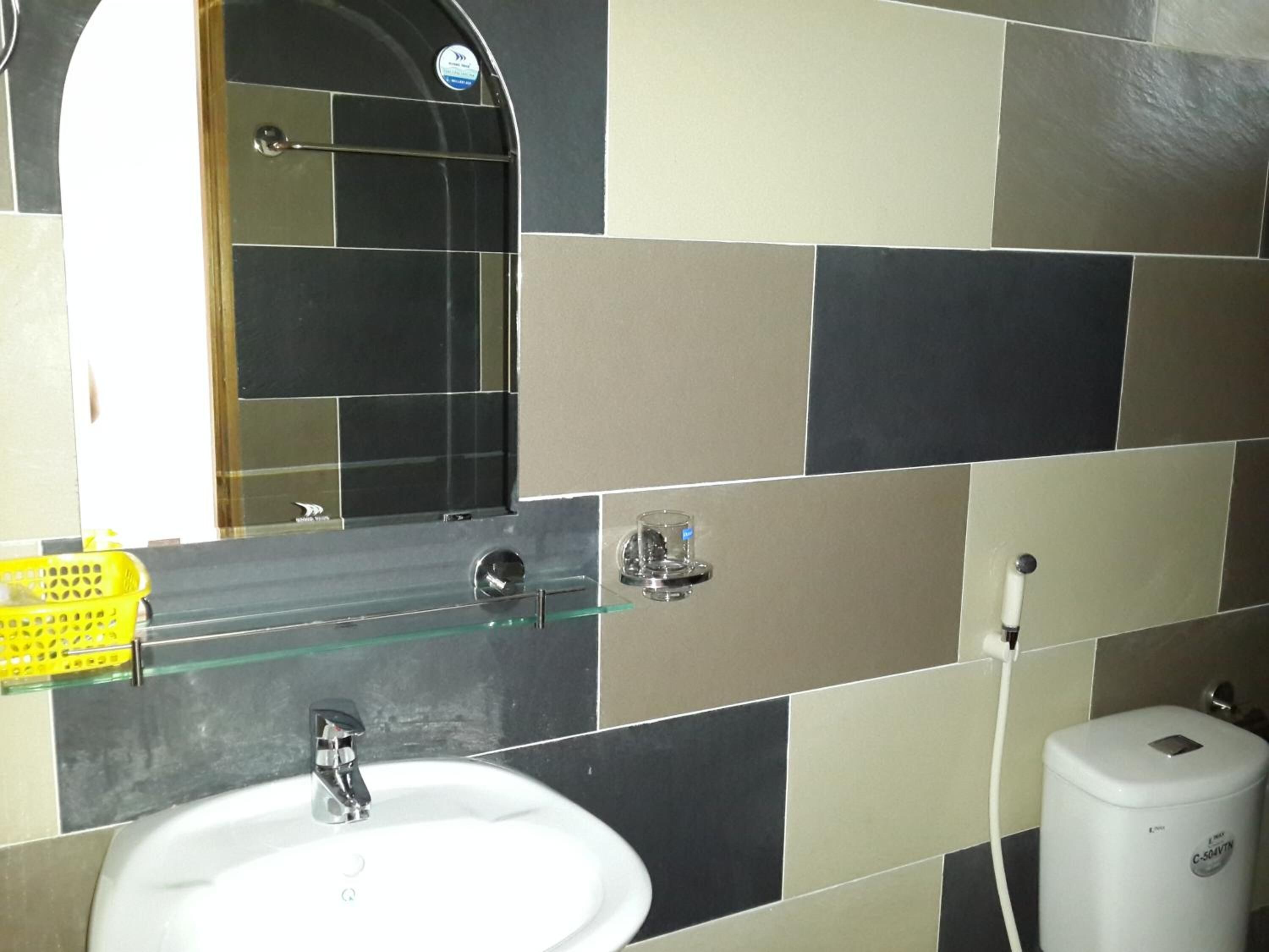 Un baño con un lavamanos blanco, un espejo y un estante de vidrio.