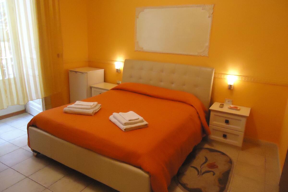Une chambre d’hôtel avec un lit, des tables de chevet, un bureau et une fenêtre avec des rideaux.
