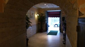 A hallway with a brick archway, a potted plant, a wall-mounted light fixture, and a door leading outside.
