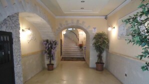 A hallway with a stone wall, a green mat, and potted plants.