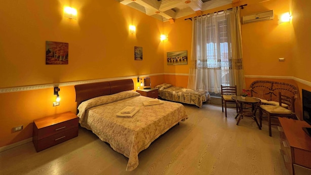 A hotel room with a bed, two bedside tables, a chair, a small table, and a window with curtains.
