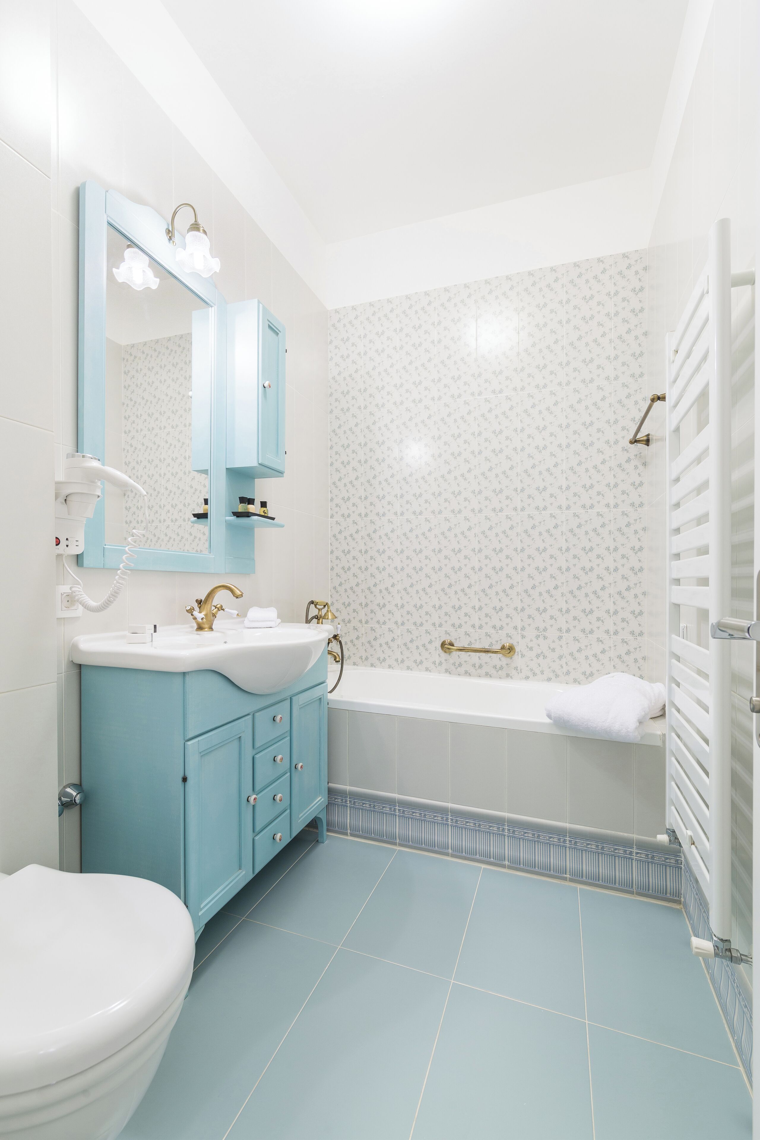 A bathroom with a white toilet, a blue vanity, a white sink, a large mirror, a bathtub, and a shower area.
