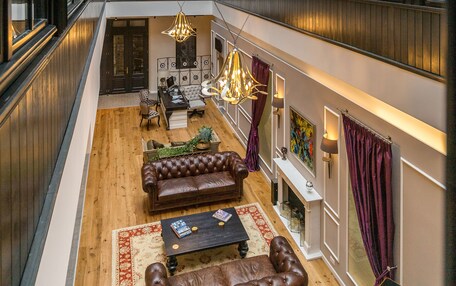 A spacious interior with a high ceiling, wooden flooring, leather sofas, a dining area, and a view through a glass atrium.