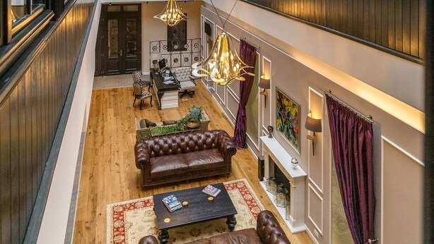 A spacious interior with a high ceiling, wooden flooring, leather sofas, a dining area, and a view through a glass atrium. - The Mansion Boutique Hotel (Bucharest)