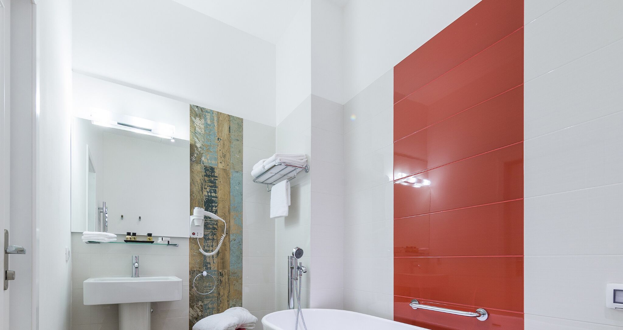 Een moderne badkamer met een witte wastafel, een spiegel, een douche met handdouche en een rode accentmuur.