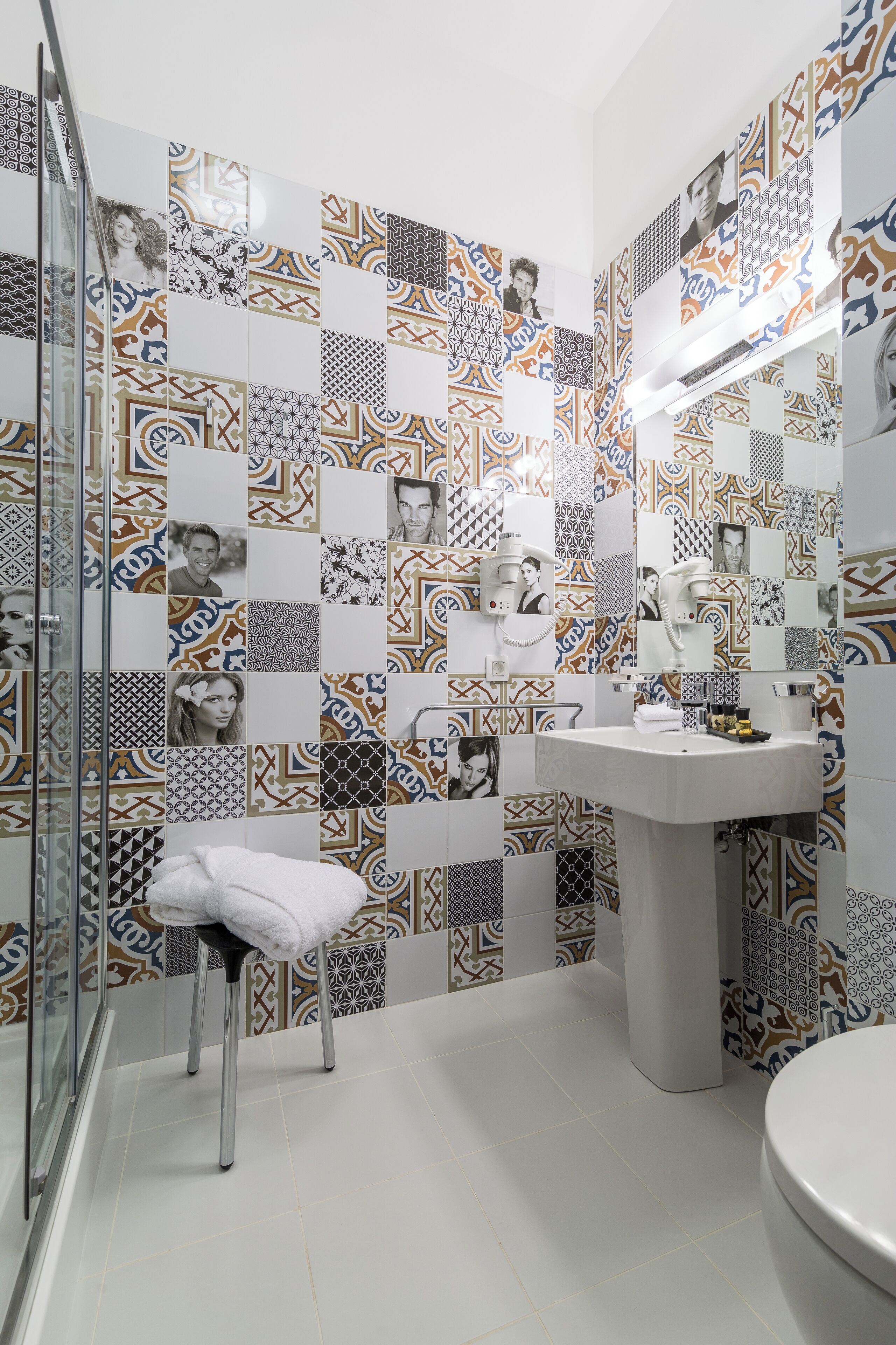 Casa de banho com azulejos estampados, lavatório e cabine de duche em vidro.